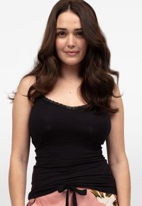 Czarna koszulka na ramiączkach z delikatnym koronkowym wyko�ńczeniem, dopasowany krój i gładka tkanina. Noszona z jasnoróżowymi wzorzystymi spodniami z troczkiem.