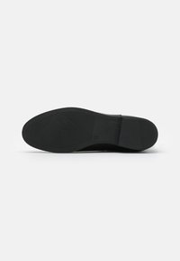 Semelle de chaussure noire avec surface en caoutchouc texturée, présentant un motif en diamant et un talon plat. Design minimaliste sans logos ni accents visibles.