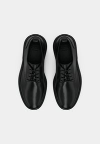 Scarpe in pelle nera con una texture liscia, caratterizzate da una punta arrotondata, un design con lacci e uno stile minimalista, viste dall'alto.