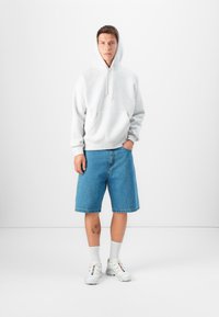 Sweatshirt cinza de algodão com um bolso frontal, combinado com calções de ganga azuis, meias brancas e ténis brancos com toques de cor.