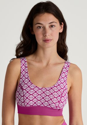 Roze sportbeha met een ronde hals en brede bandjes. Bloemenpatroon in wit en donkerder roze op een gestructureerde stof.