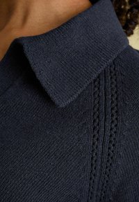 Marineblauer Strickpullover mit flachem Kragen, strukturiertem Rippstrick und dekorativen Details entlang des Halsausschnitts. Weicher, leichter Stoff.