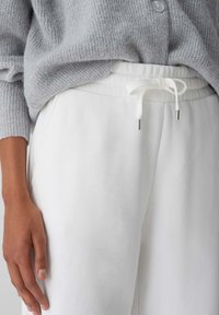 Weiße Jogginghose mit elastischem Bund, Kordelzugverschluss und silbernen Aglet, kombiniert mit einem weichen grauen Rippenpullover.