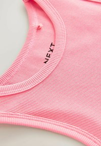 Débardeur rose à côtes avec un col rond et un détail de logo. La texture du tissu est douce et extensible, adaptée à une tenue décontractée.