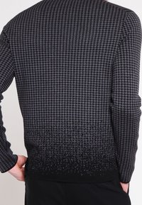 Pull-over noir et gris avec un motif pied-de-poule, un tissu texturé et un dégradé s'estompant vers un noir uni à l'ourlet.