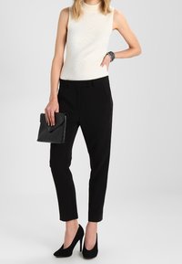 Pantalons noirs ajustés avec une jambe fuselée, associés à un haut sans manches blanc à côtes. Des escarpins noirs et une pochette noire complètent le look.