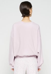 Sweat-shirt oversize rose clair avec épaules tombantes, ourlet côtelé et texture douce, associé à un pantalon clair à motif.