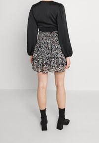 Top negro de manga larga combinado con una falda de estampado floral con volantes, botas negras hasta el tobillo con tacones de bloque y una cintura fruncida.