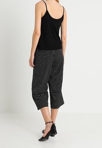 Schwarzes Tanktop kombiniert mit schwarz-weiß gestreiften Culottes, die einen entspannten Schnitt, eine kurze Länge und einen strukturierten Stoff aufweisen. Schwarze Absatzschuhe runden den Look ab.
