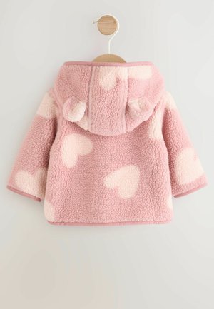 Veste en polaire rose avec des motifs en cœur blancs. Elle est dotée d'une capuche avec des oreilles, de manches longues et d'une finition douce et texturée.