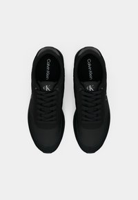 Sapatos de desporto pretos com um cabedal têxtil suave, bico arredondado e design tradicional de atacadores. Com realces discretos de marca e costura azul.