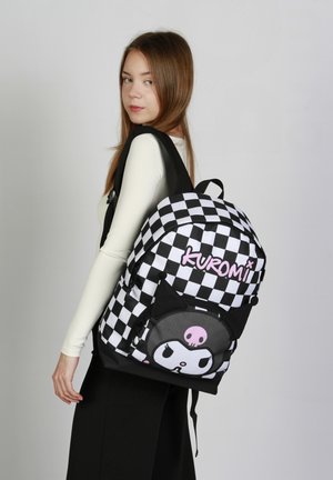 Mochila a cuadros en blanco y negro con acentos en rosa y una cara de personaje de dibujos animados, con correas acolchadas y un bolsillo frontal.