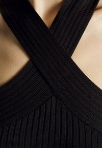 Svart ribbade halterneck-top med korsade band och en texturerad yta, som framhäver en sömlös design och en smidig linje vid halsen.