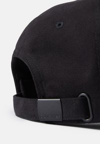 Cappello da baseball nero in tessuto strutturato. Presenta una fascia regolabile e una fibbia nera con "Calvin Klein" incisa sopra.