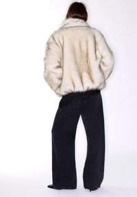 Giacca in pelliccia sintetica color crema con una texture soffice, abbinata a jeans neri a gamba larga. Il look presenta una vestibilità comoda e dettagli raffinati.