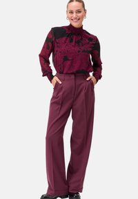 Blusa nera con motivo floreale borgogna e scollatura a balze, abbinata a pantaloni borgogna a vita alta. Tessuto liscio e vestibilità comoda.