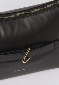 Borsa a mano in pelle nera con zip dorata e dettaglio ad gancio. Texture liscia con minimal branding e design elegante.