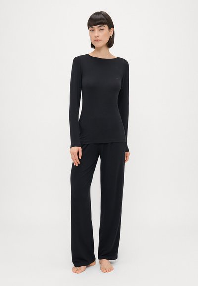 Melnas garās piedurknes krekls un atbilstošas platas bikses, kas izgatavotas no mīkstas, gludas auduma. Minimalisma stils ar smalku logo uz krūtīm.