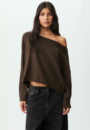 Brauner schulterfreier Pullover aus weichem Strick, im cropped Design mit langen Ärmeln. Kombiniert mit hoch taillierten schwarzen Jeans, die eine subtile Textur aufweisen.