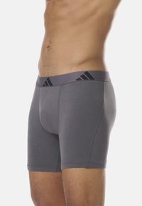 Boxers gris avec une large ceinture élastique ornée de trois bandes noires, fabriqués dans un matériau doux et extensible. Texture lisse.