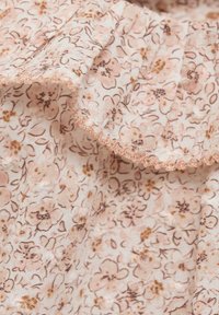 Tessuto a fantasia floreale con sfondo di un rosa tenue, decorato con fiori marroni e gialli. Bordo arricciato con un delicato profilo marrone chiaro.
