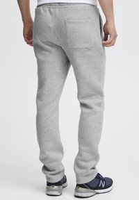 Gray sweatpants with a tapered design. Made of soft material, featuring a back pocket and elastic waistband. Paired with navy sneakers.