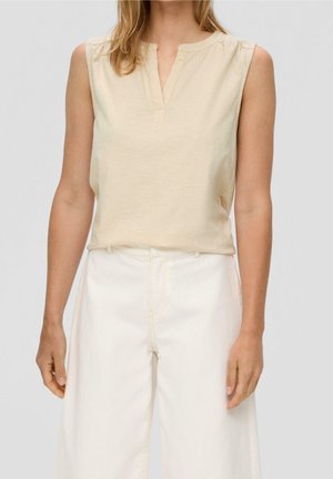 Top beige sin mangas con cuello y una tapeta parcial, con una textura suave. Combinado con vaqueros blancos de pierna ancha y cintura alta.