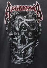 Zwart grafisch T-shirt met een schedel verweven met slangen, gedetailleerd in zwart en wit. Rode gestileerde tekst bovenaan.