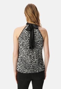 Zwart-wit haltertop met luipaardprint, geplooide textuur en een zwarte strik om de nek. Aanzicht van de achterkant, gedragen met zwarte broek.