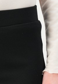 Black stretchy skirt with a smooth texture and a fitted waist. A light-colored long-sleeve top partially visible on the right.