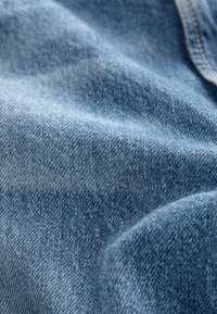 Denim tkanina u svijetlop Plavoj boji, s glatkom teksturom i blagim promjenama u nijansi, tipičnim za nošeni denim, s vidljivim uzorkom tkanja.
