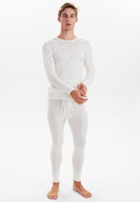 Weißes thermisches Langarmoberteil und Leggings, figurbetontes Design, weiche Textur und gerippte Bündchen. Das Oberteil hat einen Rundhalsausschnitt und ist mehrlagig gestaltet.