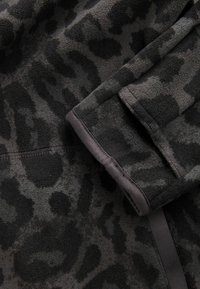 Tissu polaire gris foncé avec un motif discret de léopard noir et des finitions d'ourlet soigneusement cousues.