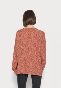 Blusa de mangas compridas em coral com padrão de leopardo preto, apresentando um corte solto e decote redondo. Tecido macio com um ligeiro brilho.
