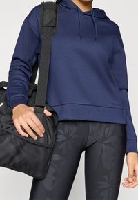 Felpa corta con cappuccio blu navy con coulisse, abbinata a leggings neri con motivo floreale e a una borsa da viaggio nera con pannelli in rete.