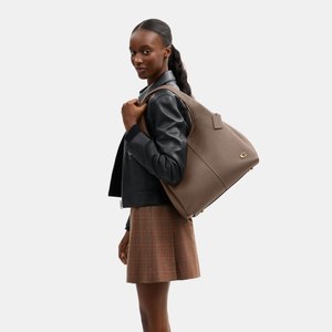 Nő fekete bőrkabátot és kockás szoknyát visel, nagy taupe színű bőr válltáskát hord aranyszínű fém díszítéssel.