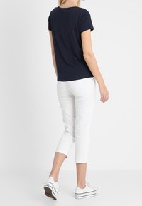 Granatowa koszulka z krótkim rękawem, miękka tkanina, luźny krój, zestawiona z białymi spodniami typu crop i białymi sneakersami, prosty i swobodny design.