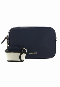 Marineblå skinn crossbody-veske med strukturert finish, gullfarget maskinvare og en kontrasterende mønstret stropp med svart og hvit design.