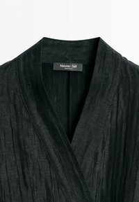 Zwart getextureerd kledingstuk met kraag en een kruisvormige voorhalslijn, met een Massimo Dutti-label dat binnenin de kraag is genaaid.