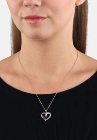Collana con pendente a forma di cuore in oro rosa, caratterizzata da un design a foglia testurizzato e una sezione decorata con pietre trasparenti su una metà, sospesa a una catena sottile.