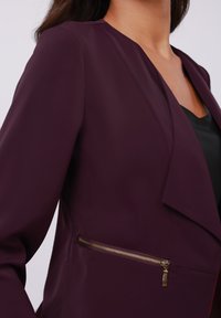 Lilla bleiser, millel on sile kangas ja kihiline krae disain. Küljel on detailiks kuldse riistvara ja lukuga tasku.