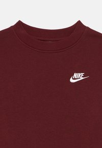 Bordó pulóver, bordázott kerek nyakkal, bal mellen fehér hímzett Nike logóval, sima textúrával.