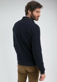 Pull bleu marine avec un col et des poignets côtelés, présentant une subtile touche d'orange. Design ajusté et texture douce.