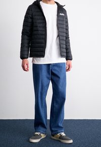 Czarna kurtka puchowa z poziomym przeszyciem, z przodu zamek błyskawiczny i kaptur; pod spodem biała koszulka; niebieskie spodnie o szerokich nogawkach; szaro-beżowe sneakersy.