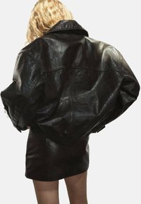 Chaqueta de cuero negra con un silueta oversize, hombros anchos y detalles de textura sutiles. Presenta acentos de cremallera y una cintura elástica.