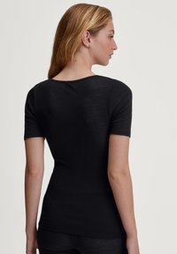 Zwart ribbed top met korte mouwen en een ronde hals. De stof lijkt zacht en heeft een getailleerde pasvorm die de vorm van het lichaam benadrukt.