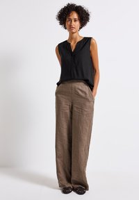 Blouse sans manches noire avec un col en V et des détails de boutons, associée à un pantalon en lin beige clair à coupe large et des chaussures noires tressées à enfiler.