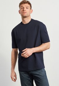 Námořnická modrá bavlněná t-shirt s krátkým rukávem a kulatým výstřihem, s volným střihem a jemnou texturou. Nosit s tmavými džíny.