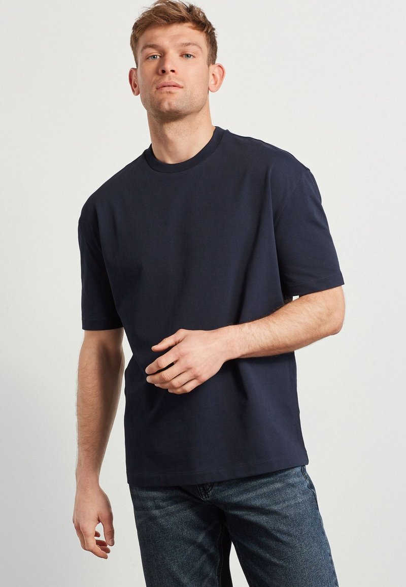 Námořnická modrá bavlněná t-shirt s krátkým rukávem a kulatým výstřihem, s volným střihem a jemnou texturou. Nosit s tmavými džíny.
