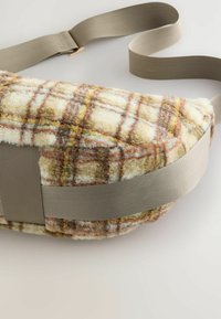 Miękka torebka na ramię z żółto-brązowo-beżowym wzorem w kratkę. Szary regulowany pasek oraz miękka, teksturowana tkanina o zaokrąglonym kształcie.